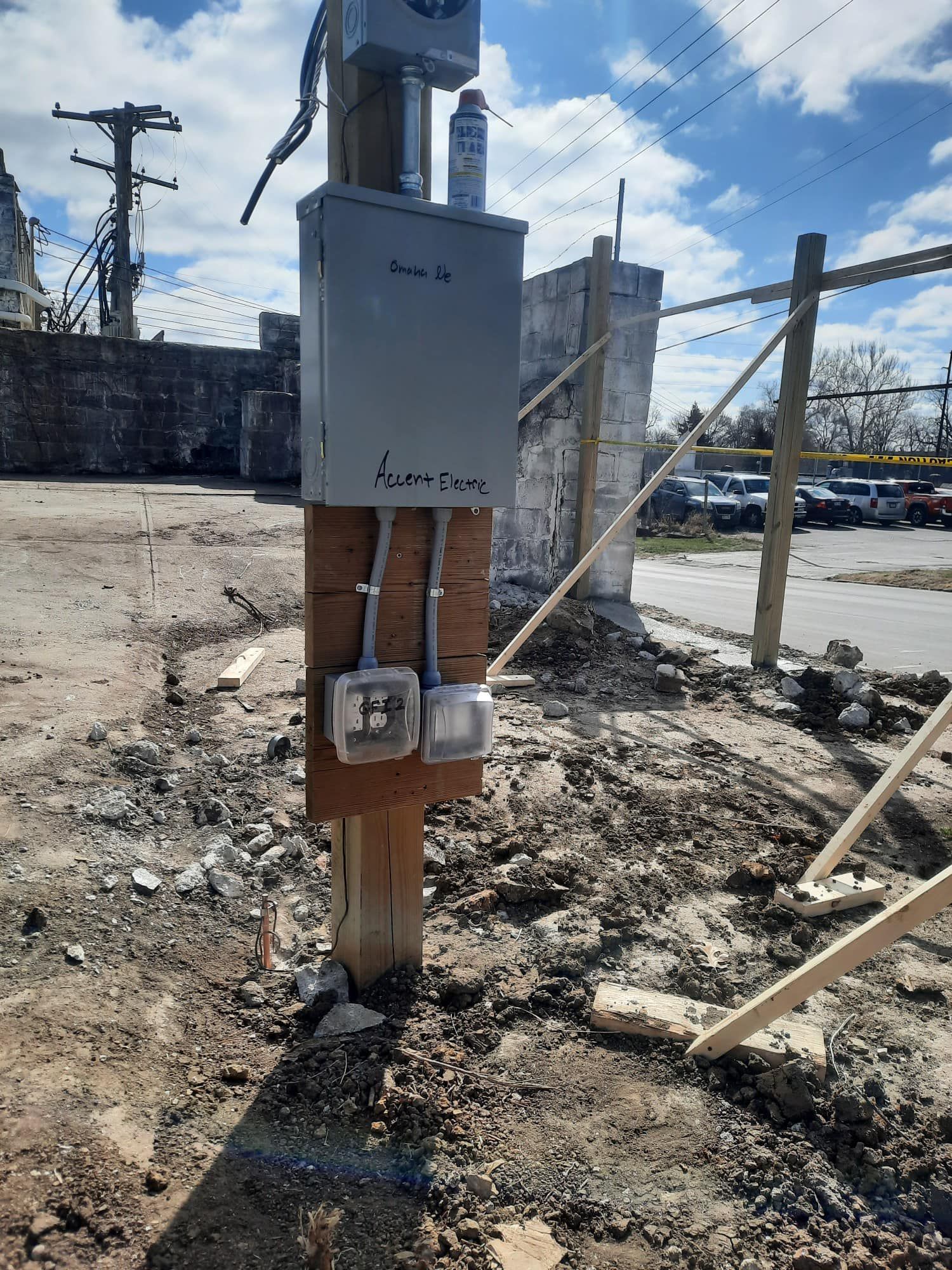 An electrical panel mounted on a wooden post in an open, dirt-covered construction site under a blue sky.