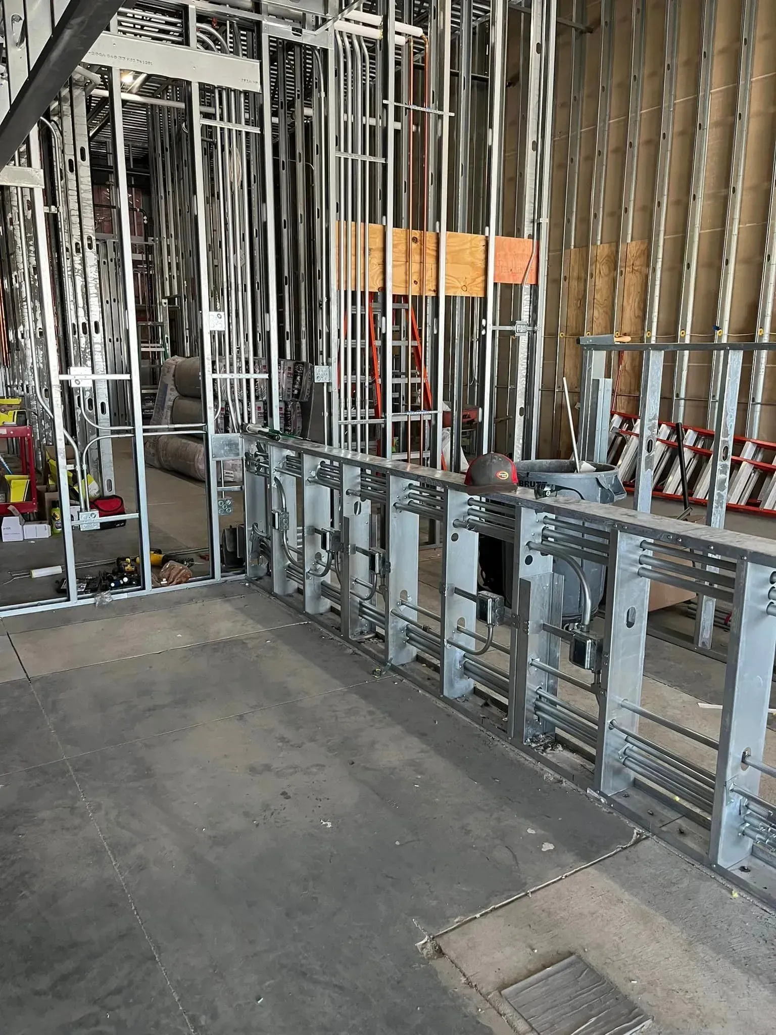Interior construction site showing metal wall framing studs and electrical conduit installed along a base partition.