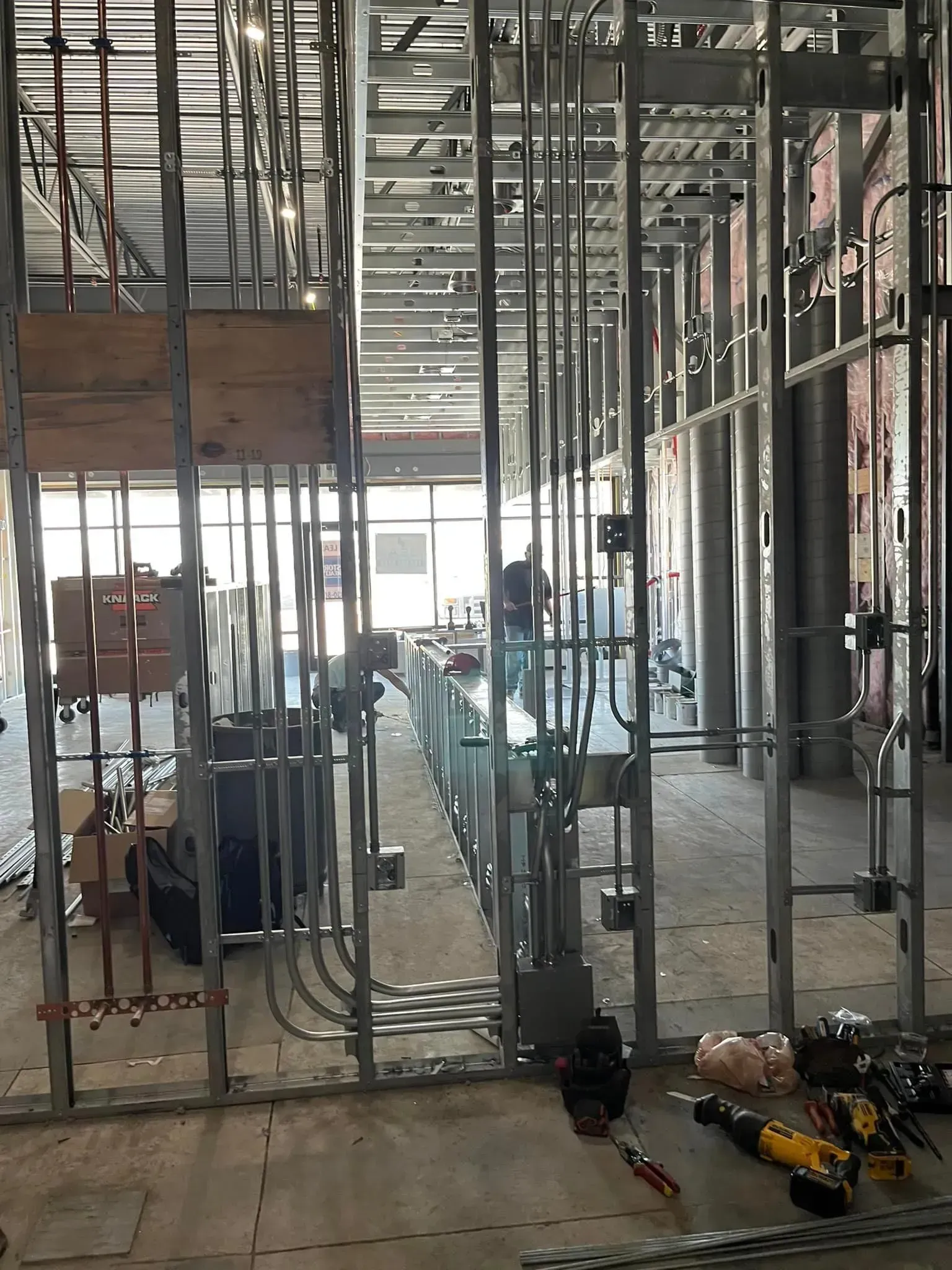 An interior construction site featuring metal wall studs, electrical conduits, and junction boxes in a room under renovation.