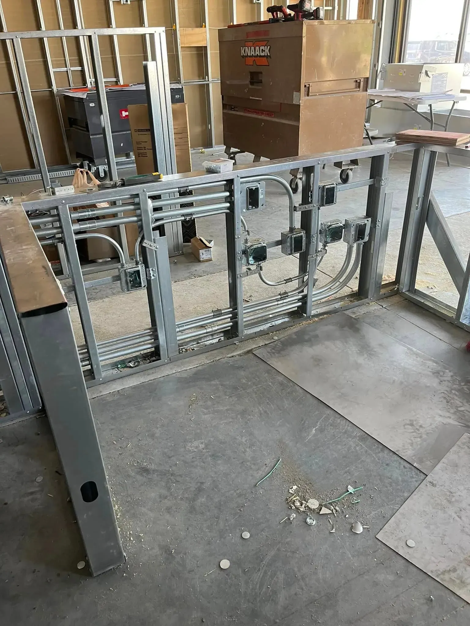 Construction site interior showing metal wall framing with electrical conduits and outlet boxes installed.