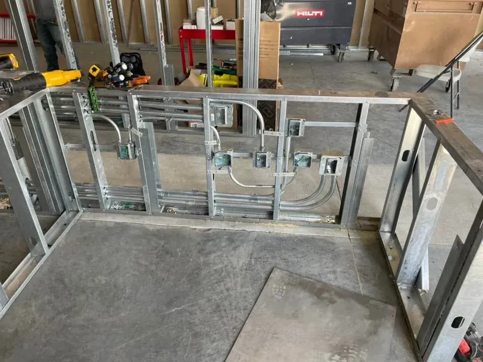 Interior metal framing for a wall under construction with electrical junction boxes and conduits installed.