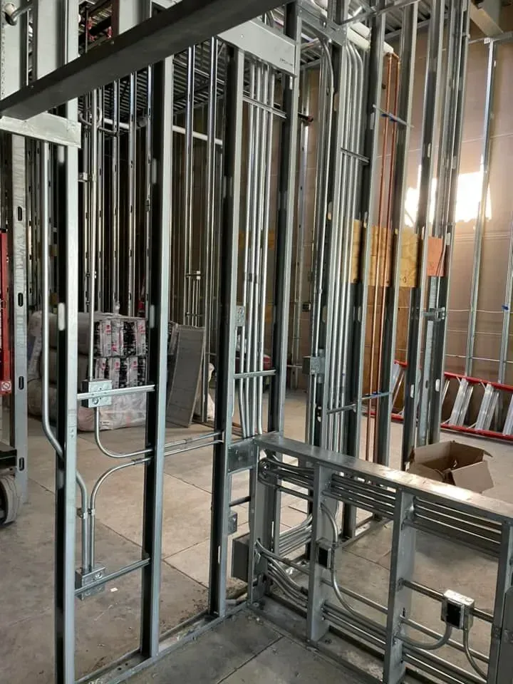 Interior construction site showing metal wall studs with installed electrical conduit and boxes.