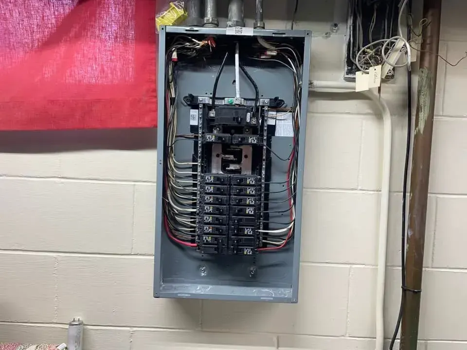 An open electrical breaker panel box mounted on a white cinder block wall.