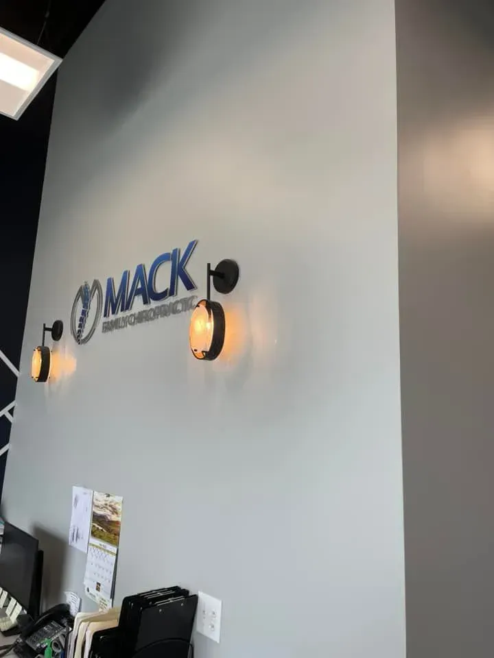 A reception area wall with the “MACK CHIROPRACTIC” logo, illuminated by two round, bronze-toned wall sconces.