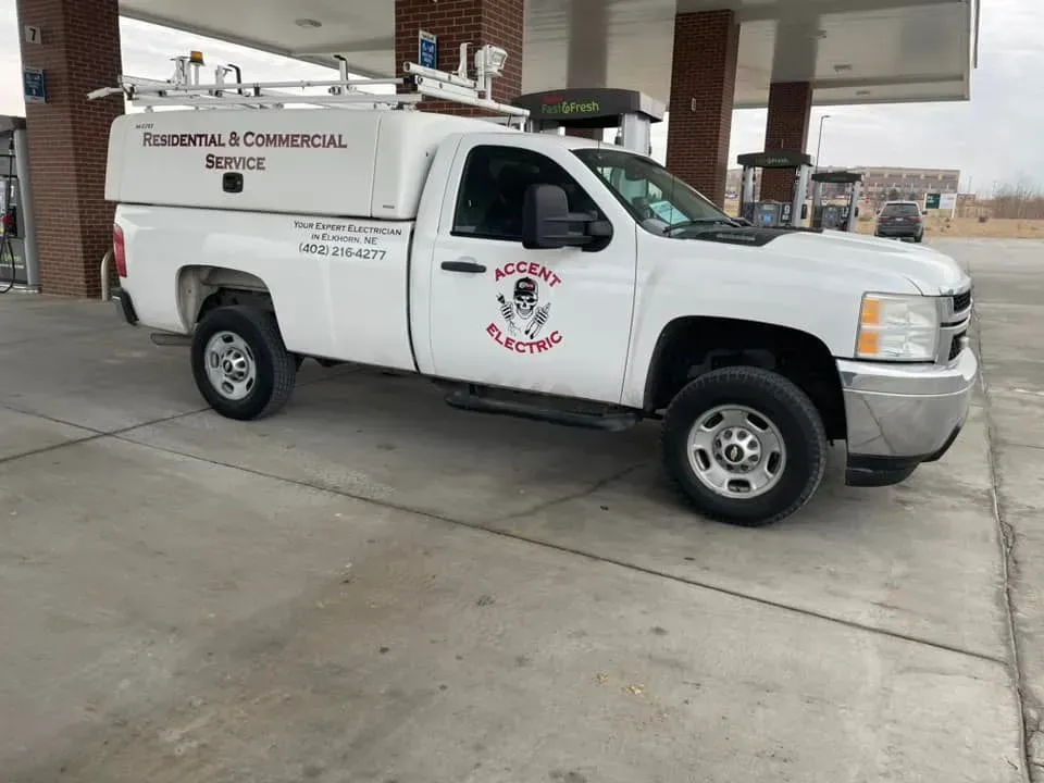 A white Accent Electric service truck parked under the canopy of a gas station.