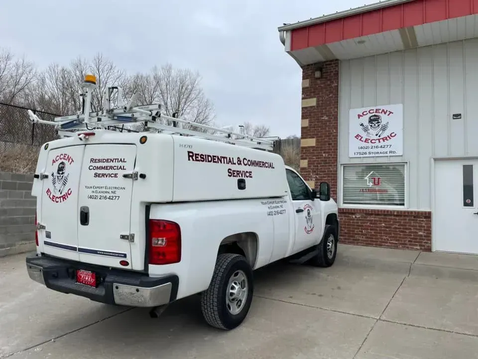 A white utility truck for Accent Electric parked in front of a brick and metal industrial building.