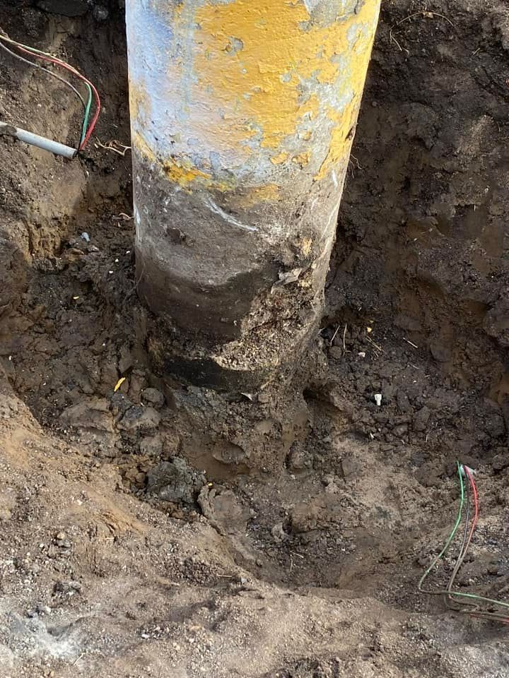 A yellow utility pole post emerges from an excavated, dirt-filled hole in the ground, showing signs of surface decay.