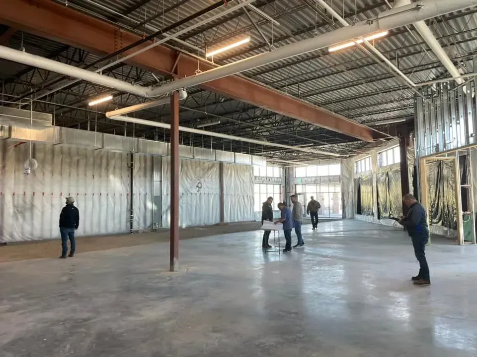 Several people stand in an unfinished, open-plan commercial building with exposed ceiling beams and insulation panels.