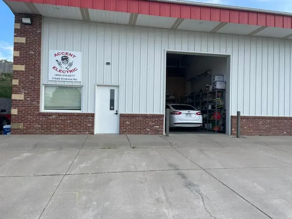 A white commercial building with a red roof, brick trim, a white door, and an open garage bay containing a white car.