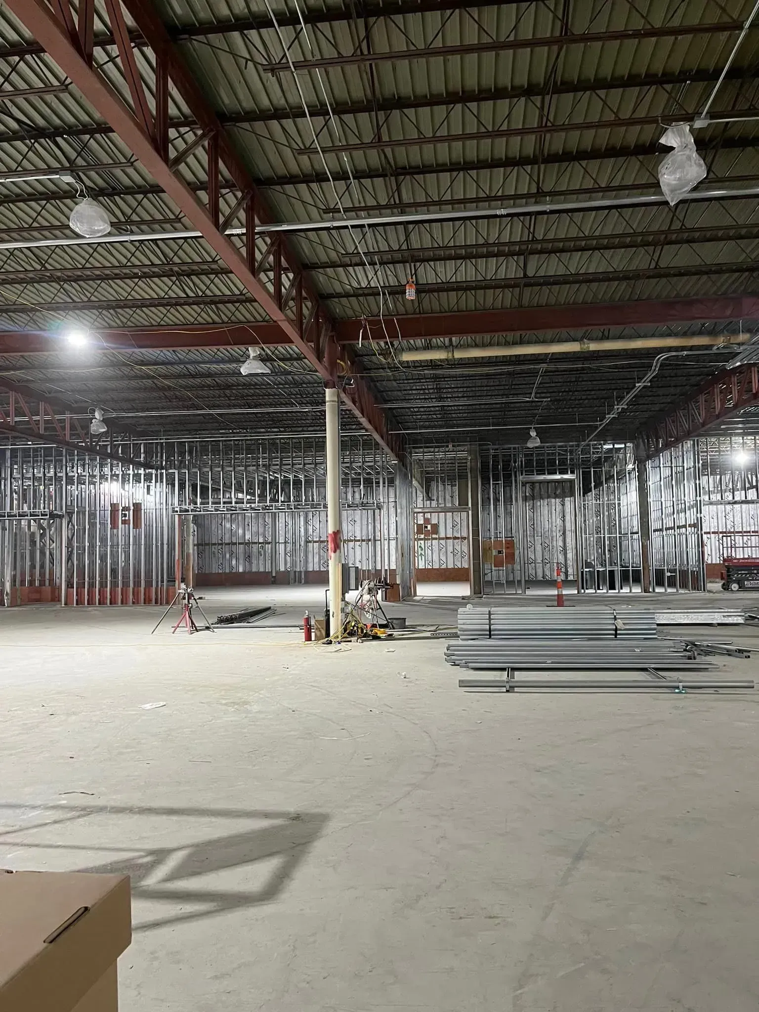 An interior construction site featuring steel framing, an exposed metal ceiling, and stacks of metal building materials.
