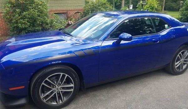 A blue dodge challenger is parked in a driveway in front of a house.