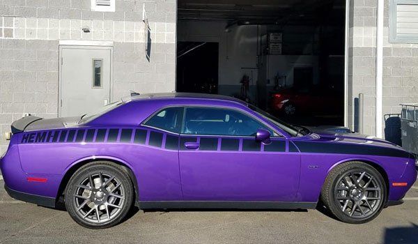 A purple dodge challenger is parked in front of a garage door.