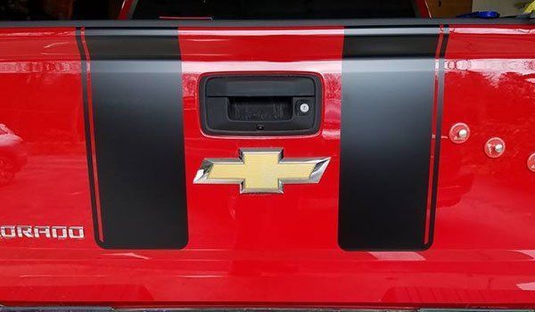 The back of a red chevrolet silverado with black stripes on it.