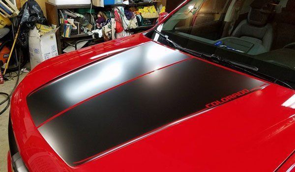 A red car with a black hood stripe is parked in a garage.