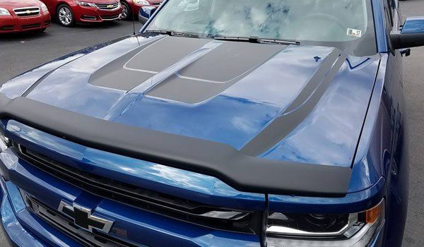 A blue truck with a black hood protector is parked in a parking lot.