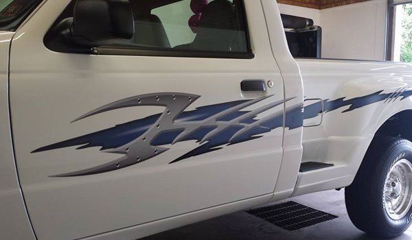 A white truck with a blue and silver design on the side is parked in a garage.