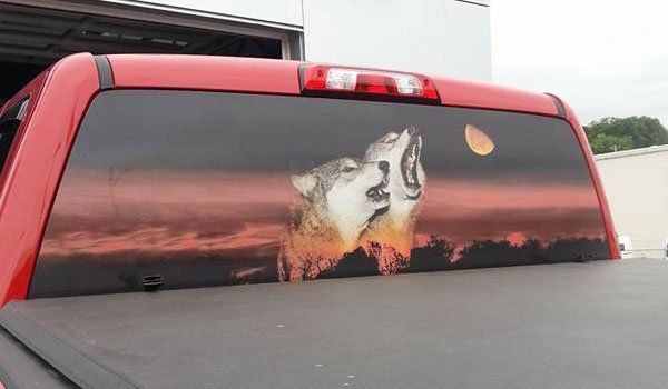 A red truck with a picture of two wolves howling at the moon on the back window.