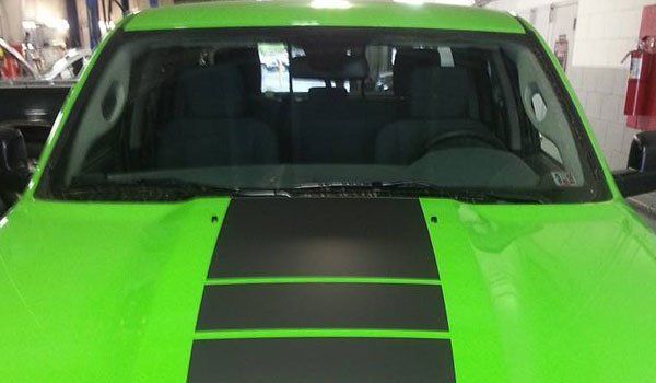 A green truck with black stripes on the hood is parked in a garage.