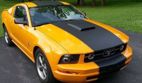 A yellow mustang with black stripes is parked in a driveway