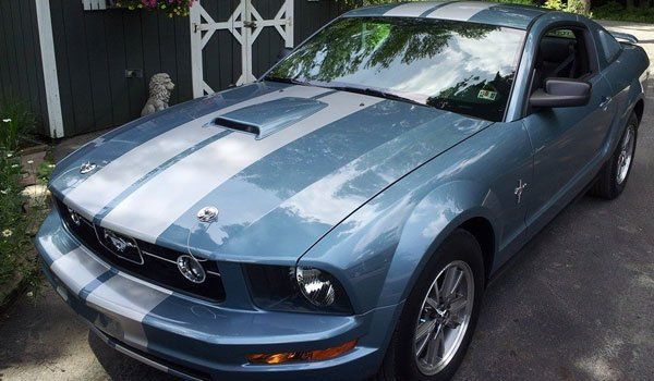 A blue mustang with white stripes on the hood is parked in a driveway.