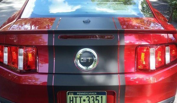 The back of a red ford mustang with black stripes and a license plate.