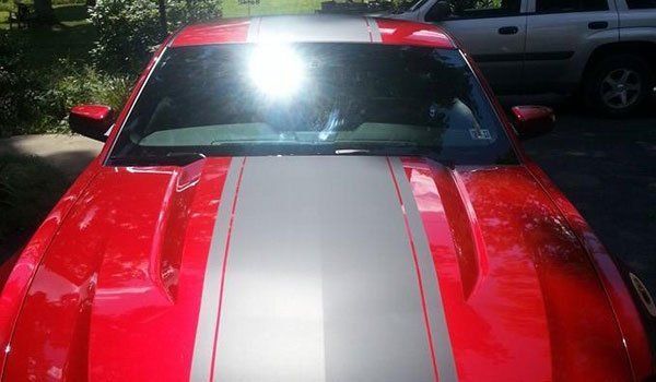 A red car with white stripes on the hood is parked in a driveway.