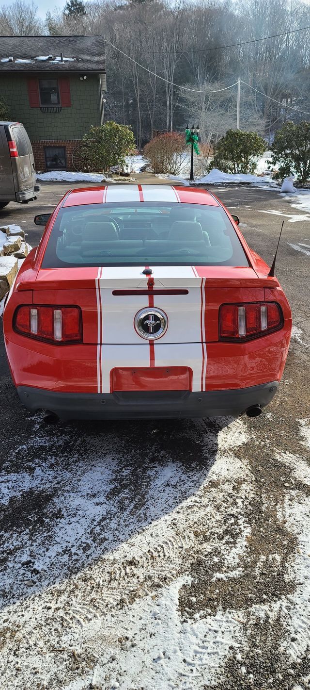 A red and white ford mustang is parked in a snowy parking lot.