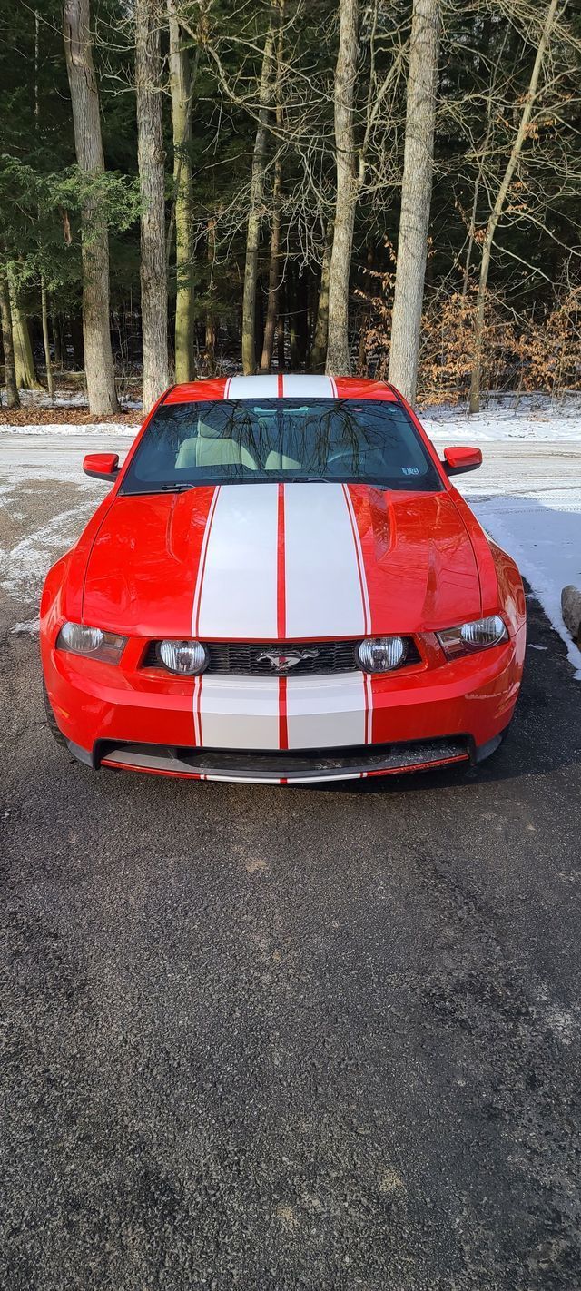 A red and white mustang is parked in a snowy parking lot.
