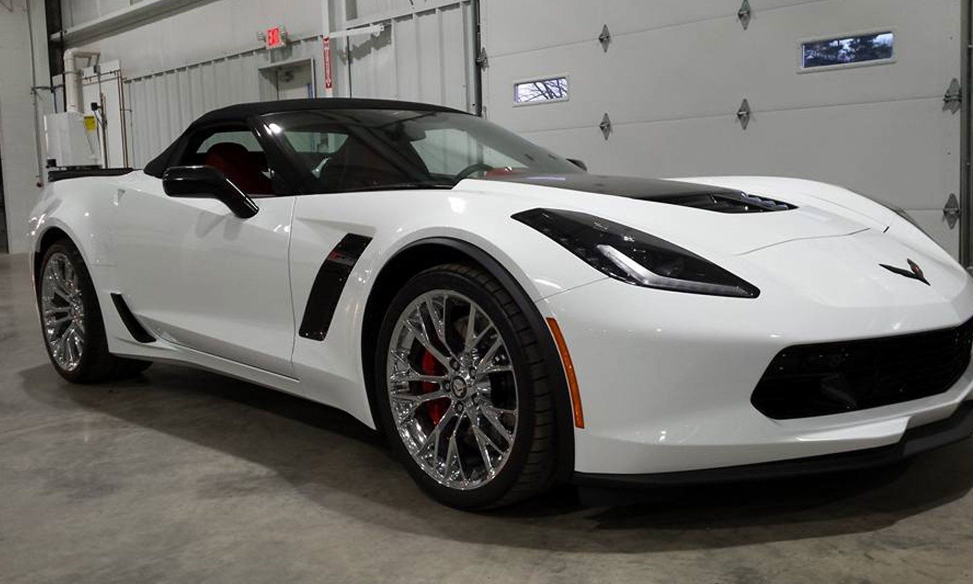 A white corvette is parked in front of a garage door.