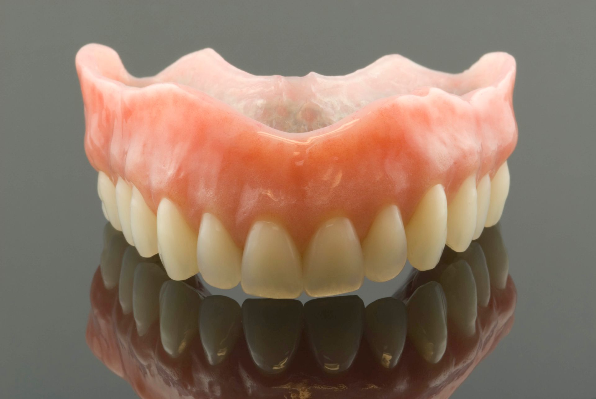 False teeth, artificial upper denture, with pink gums and white teeth, reflected on a dark surface.