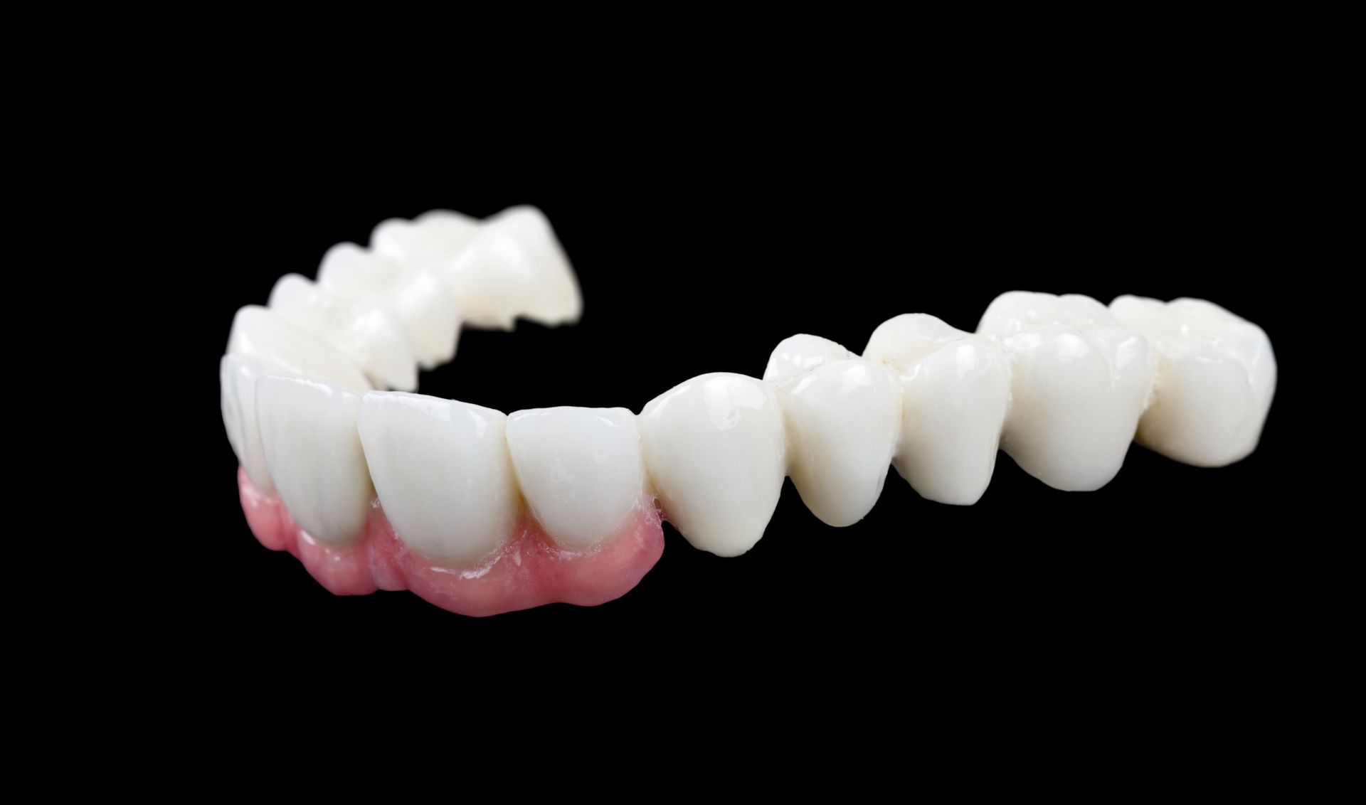 Partial dental bridge, white teeth attached to pink gums, against a black background.