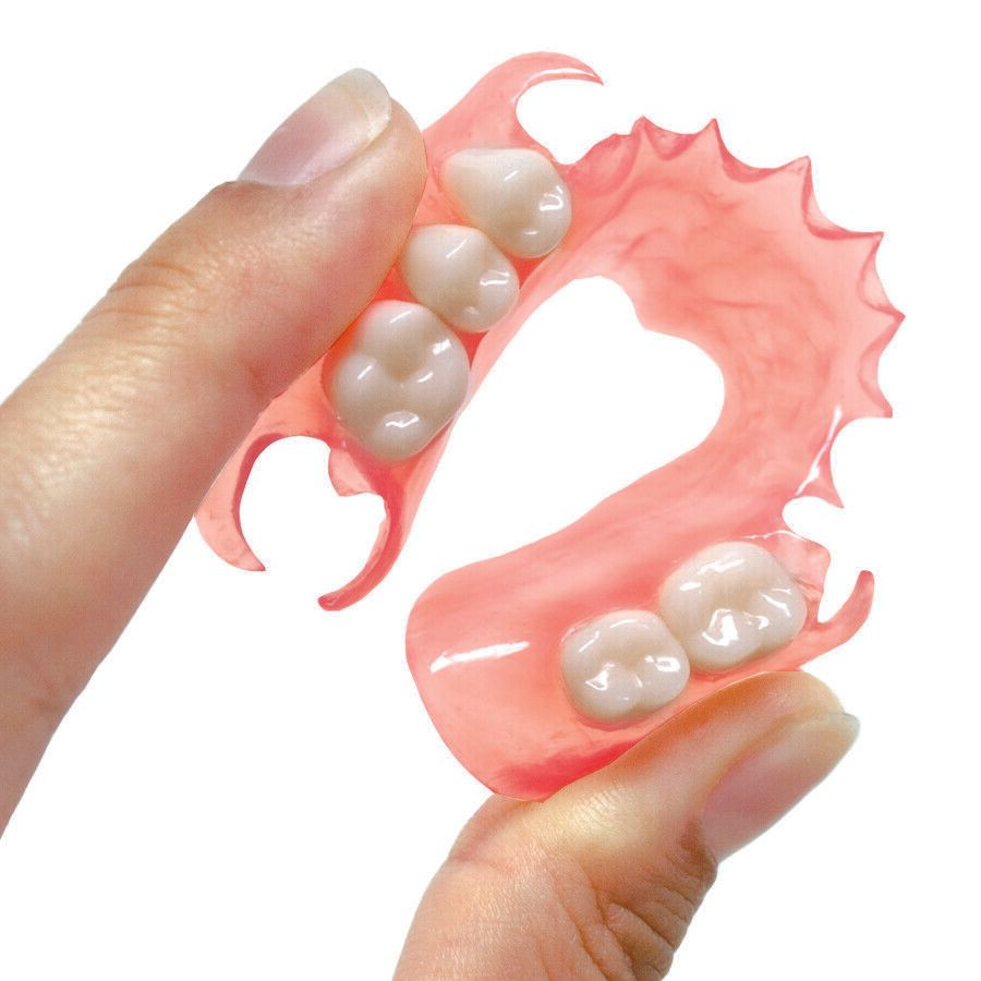 Hand holding a pink partial denture with four artificial teeth.
