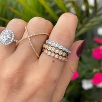 Hand wearing multiple rings: a diamond engagement ring, a cross-over band, and two bezel-set eternity bands.
