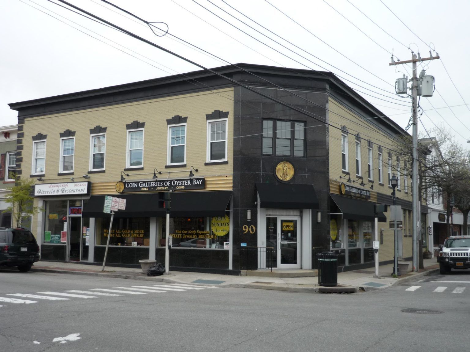 Corner street view of a tan brick storefront building with black awnings and utility lines overhead
