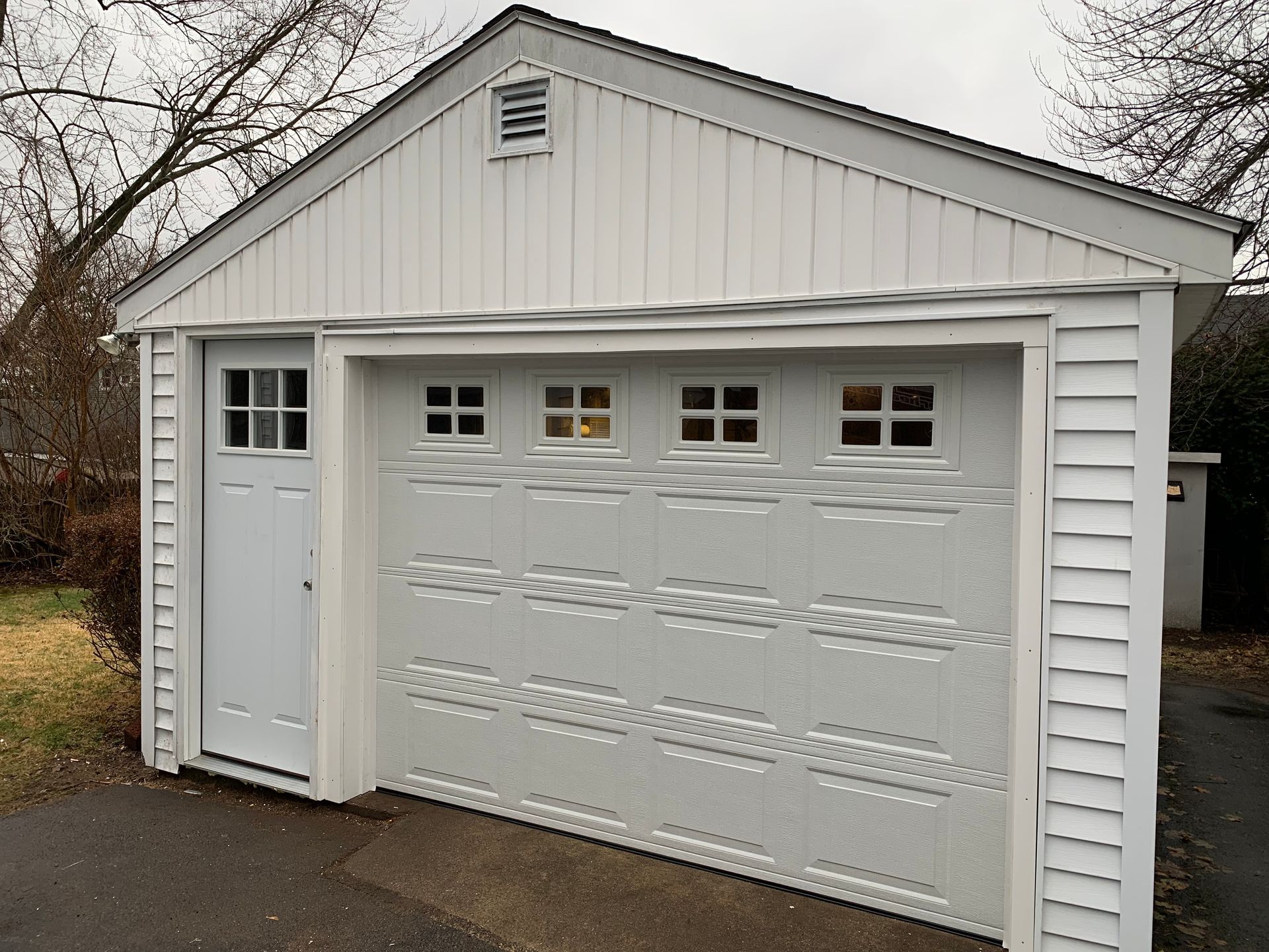 White garage with a door, driveway, and white siding.