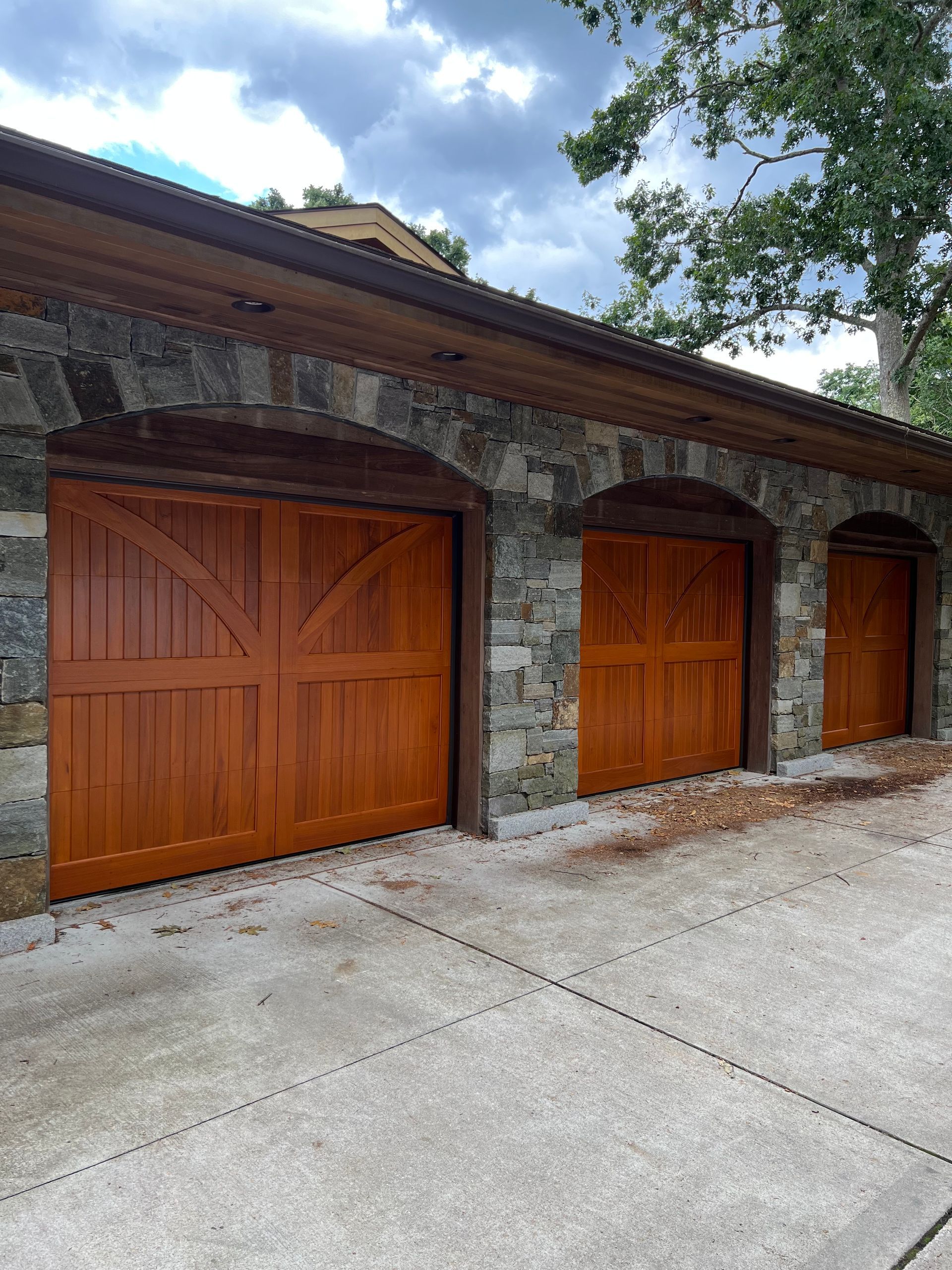 Stone facade garage with three arched wooden doors. Brown and grey color scheme.