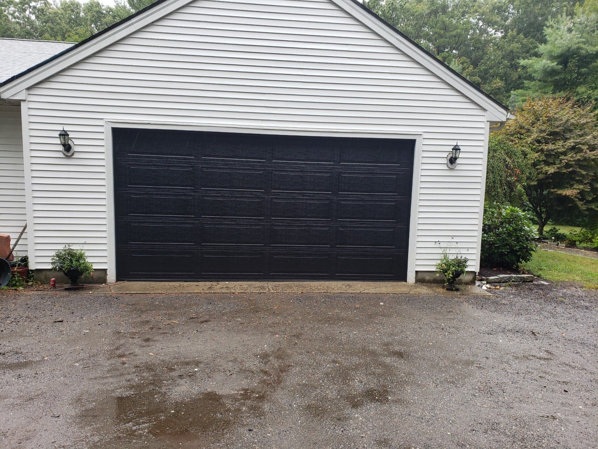 Black garage door on a white house, gravel driveway.
