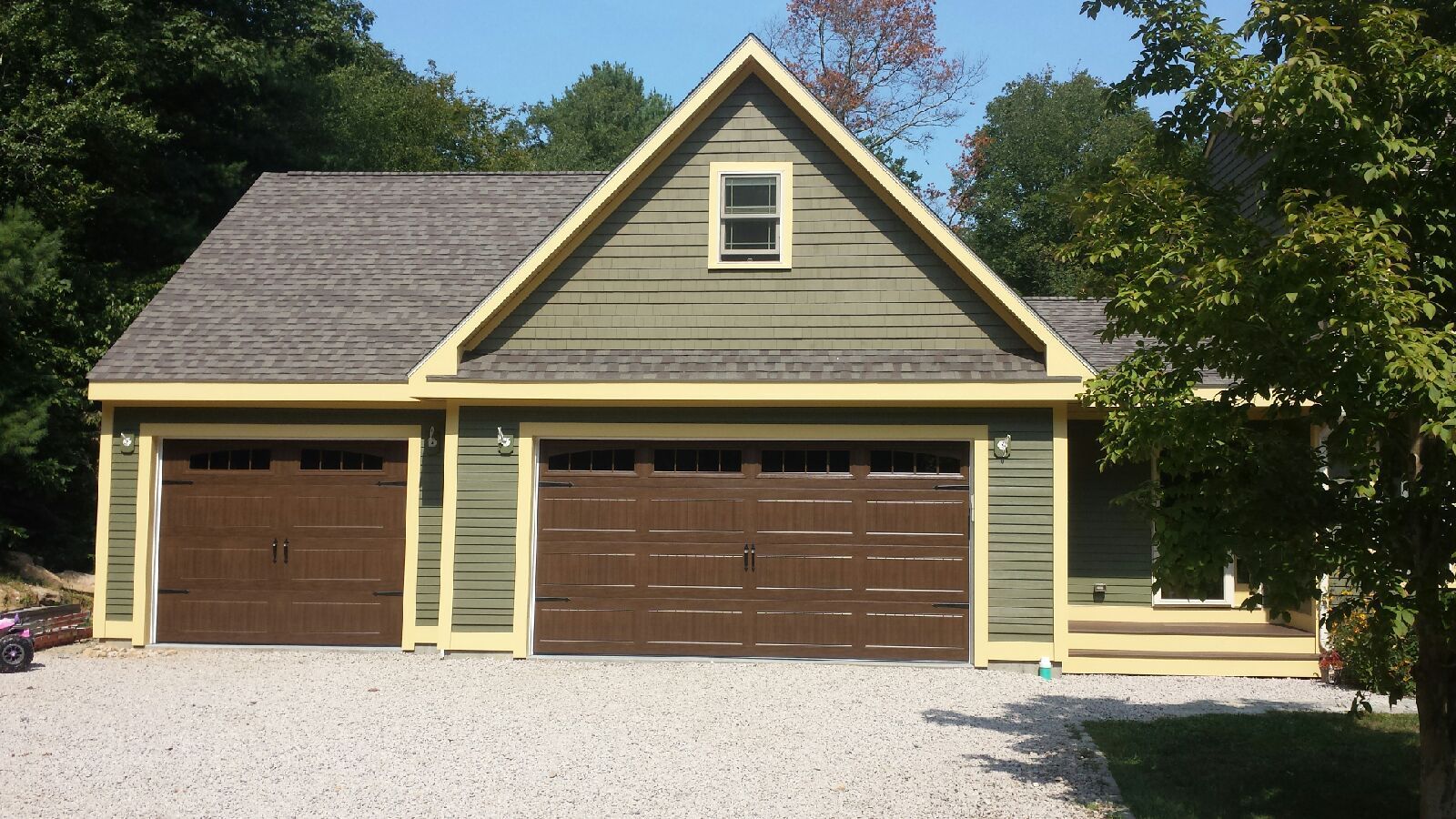 Green and brown two-car garage with a gravel driveway and small window on the gable.