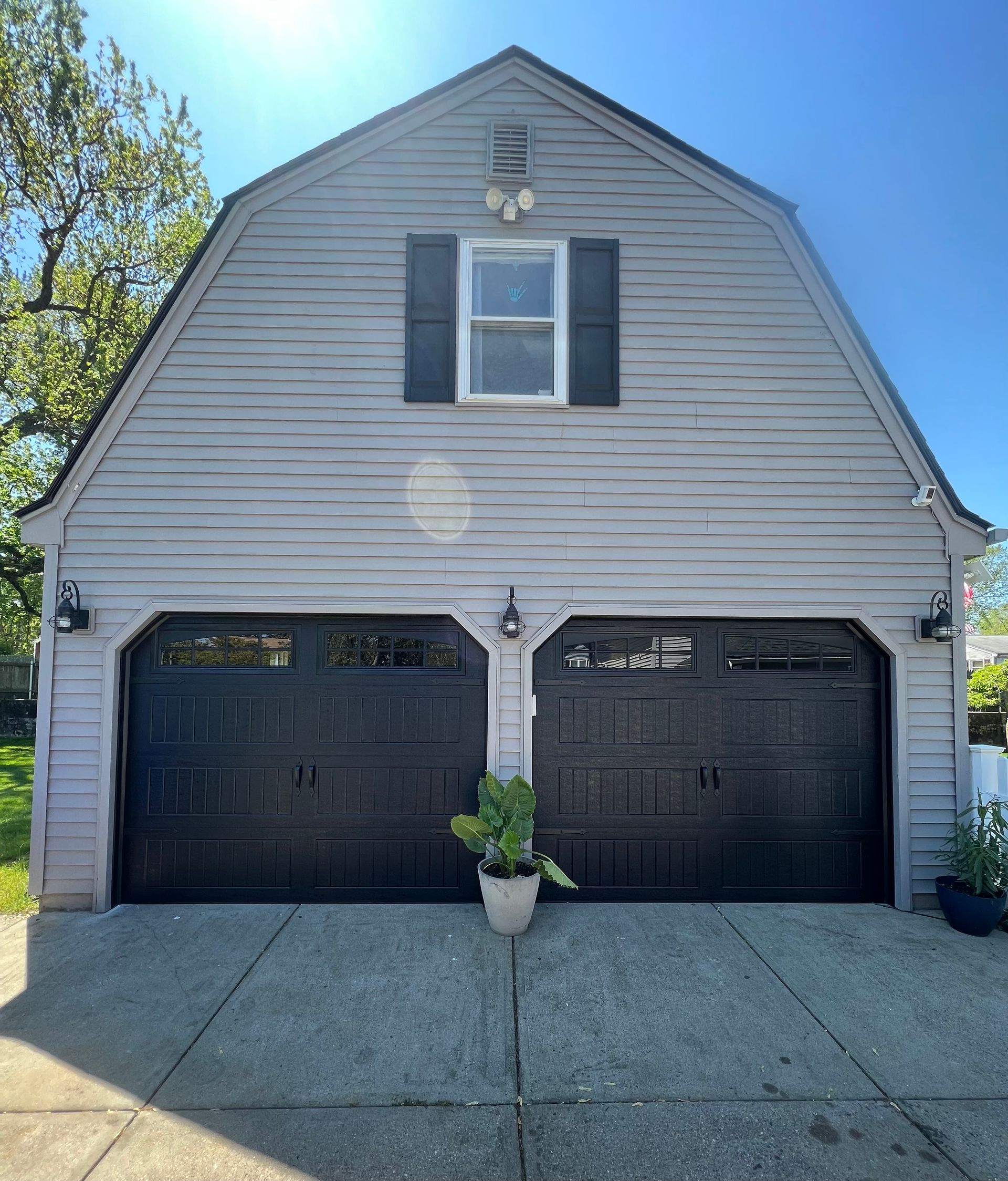 Two-car garage with black doors, gray siding, and a small window under the gable roof.