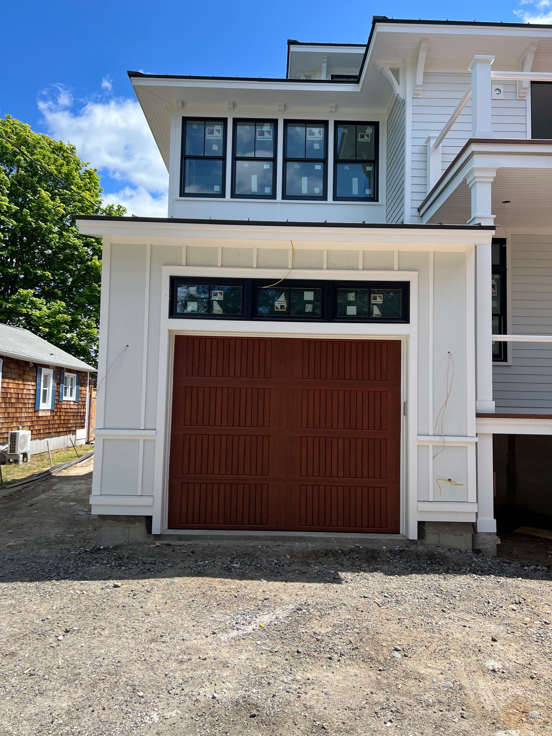 White two-story house with a brown garage door and black-framed windows, against a blue sky.