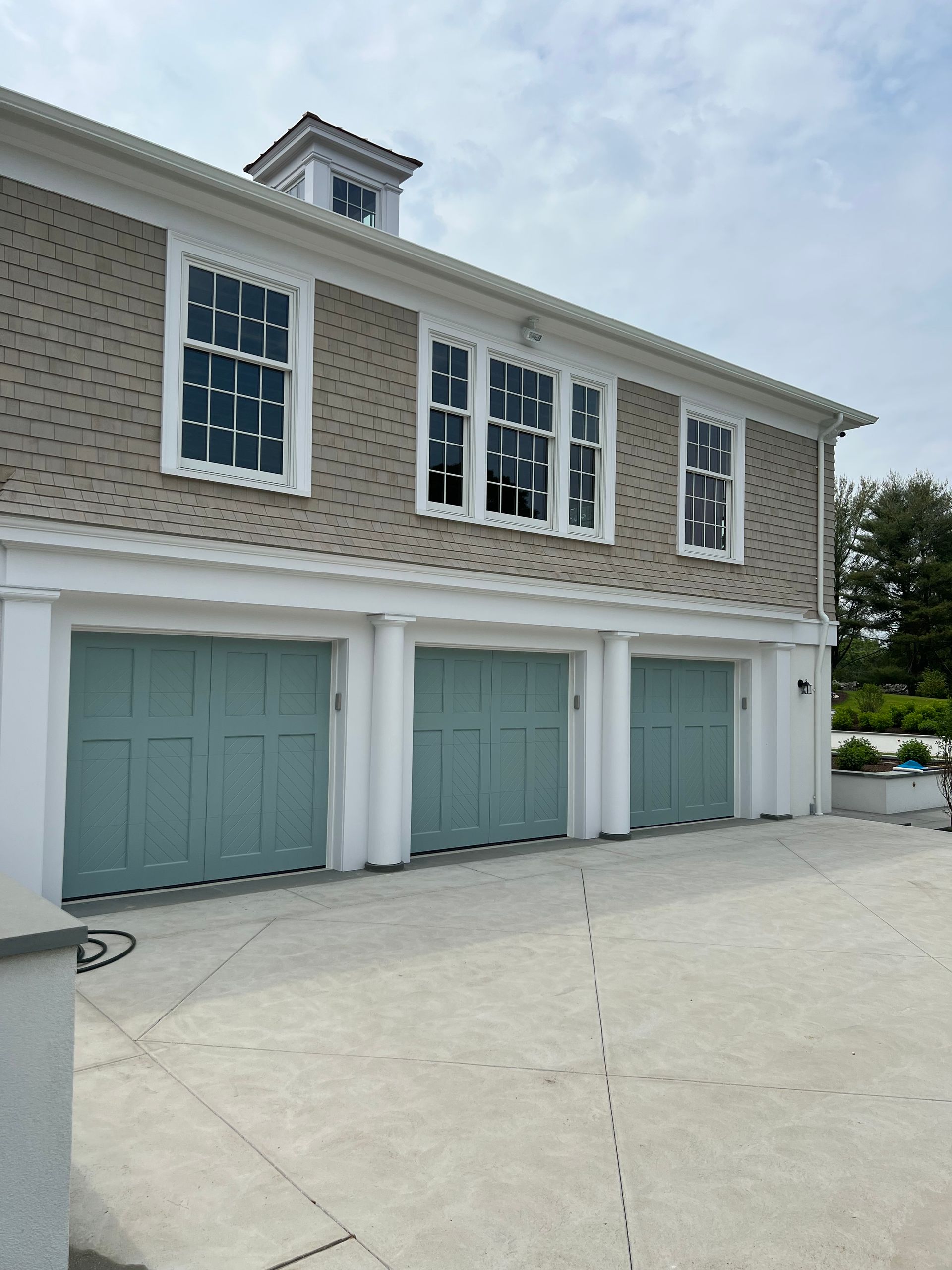 Three-car garage with light blue doors and windows above, light brown siding, and white trim.