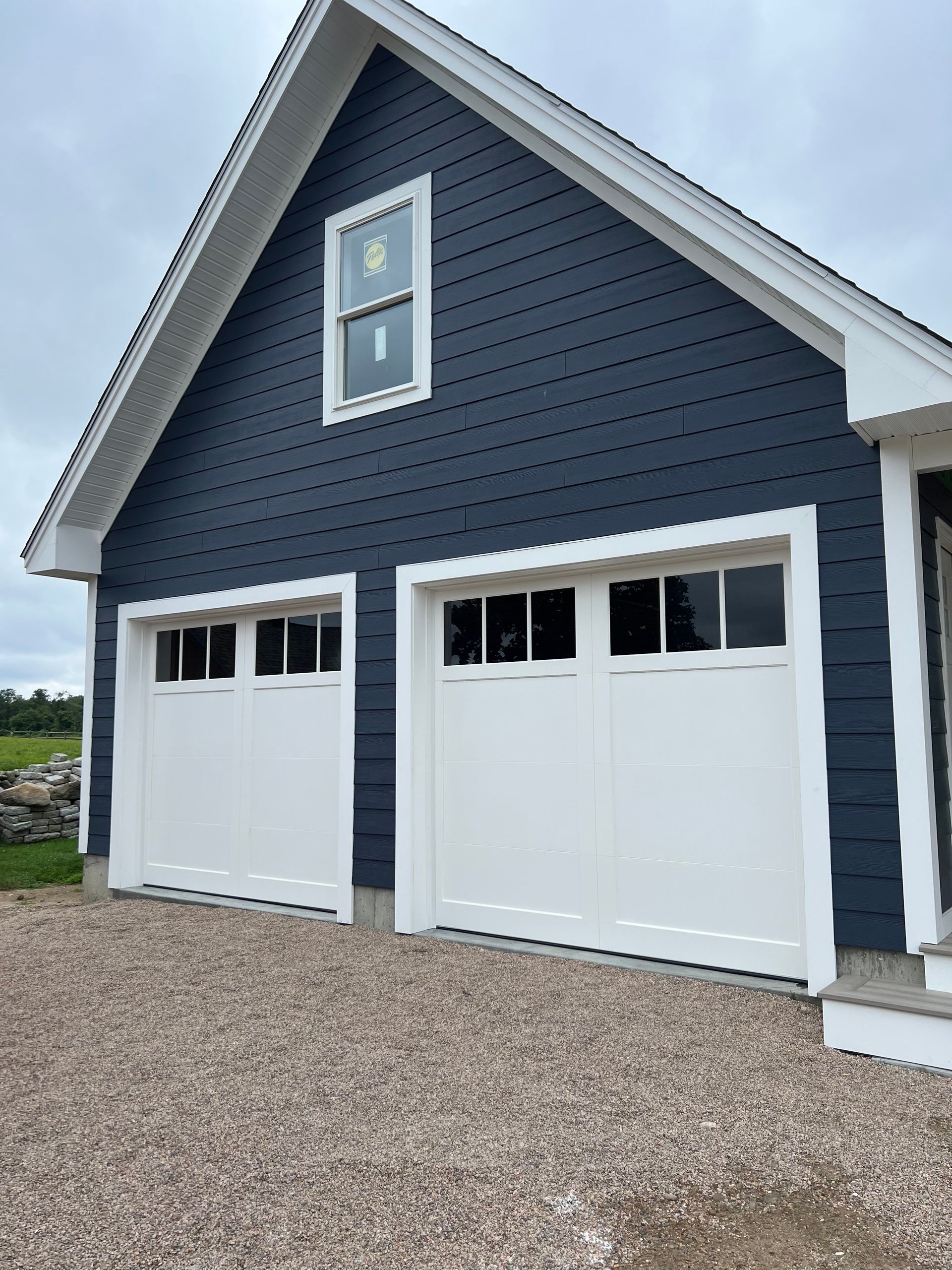 Two-car garage with white doors and trim, blue siding, and small window above. Gravel driveway.