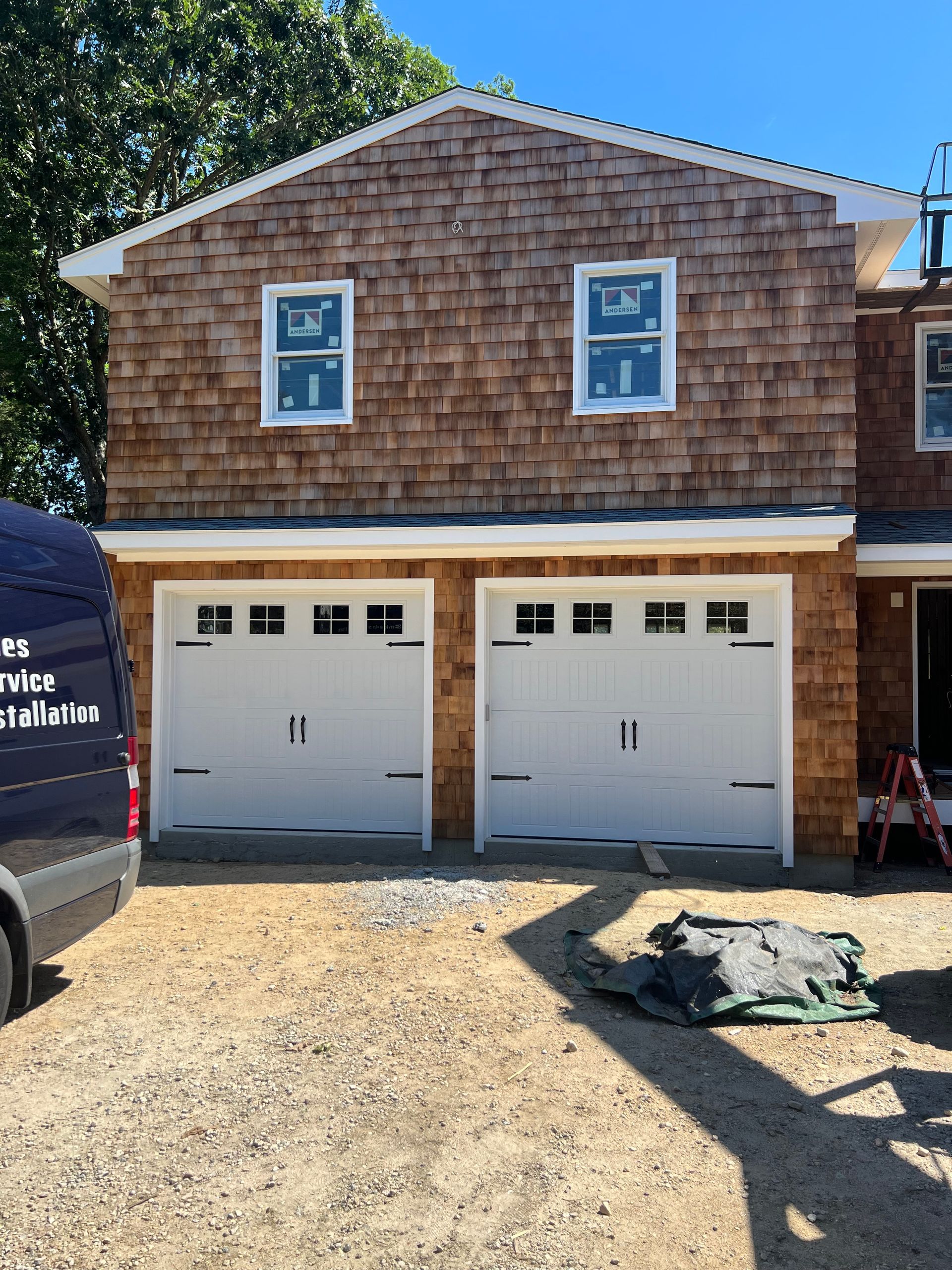 Two-story building with a garage. White garage doors below, brown shingled siding above. Two white windows on the second story.