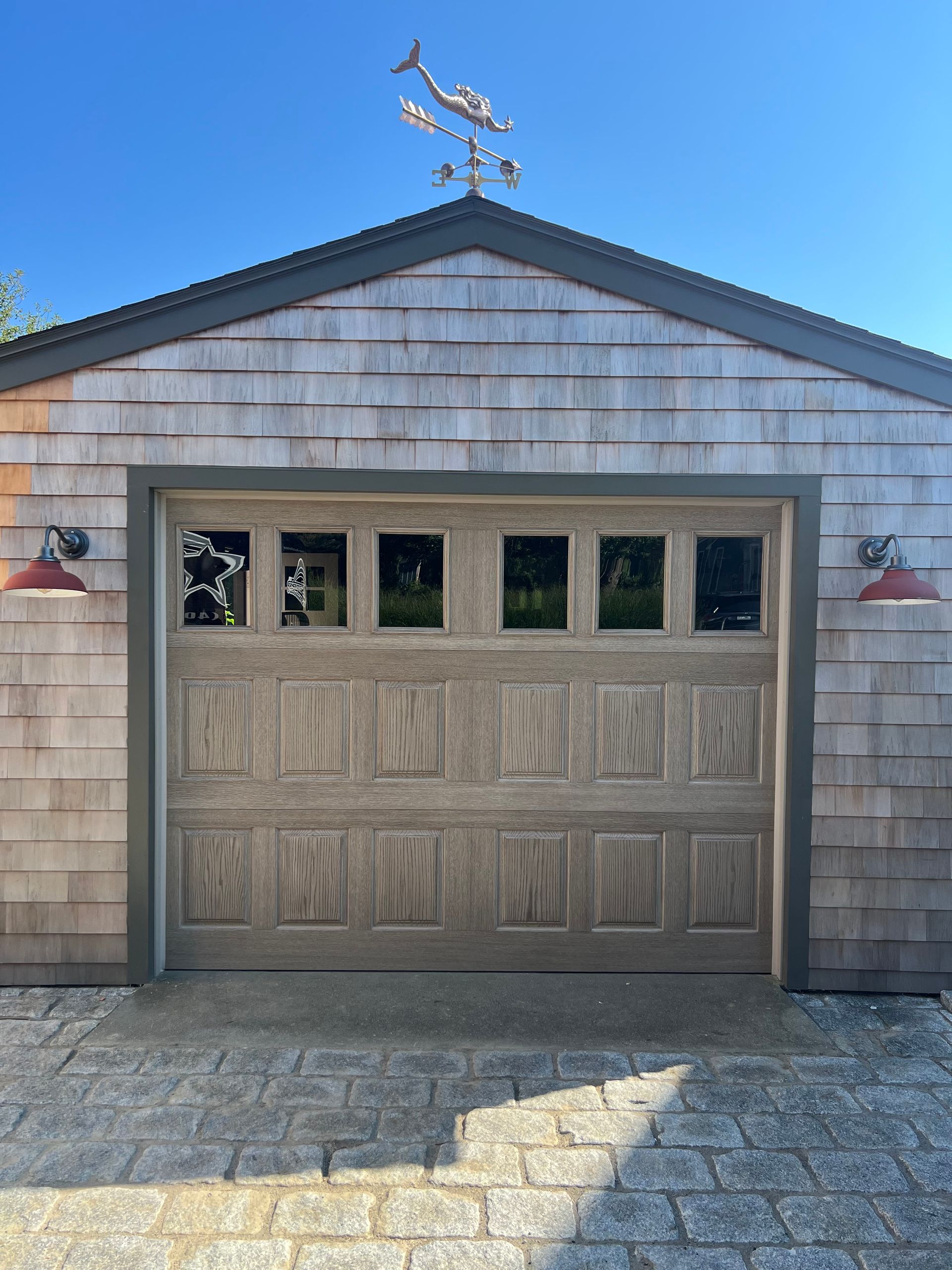 Garage with weathered wood siding and gray door, topped with a whale weathervane.