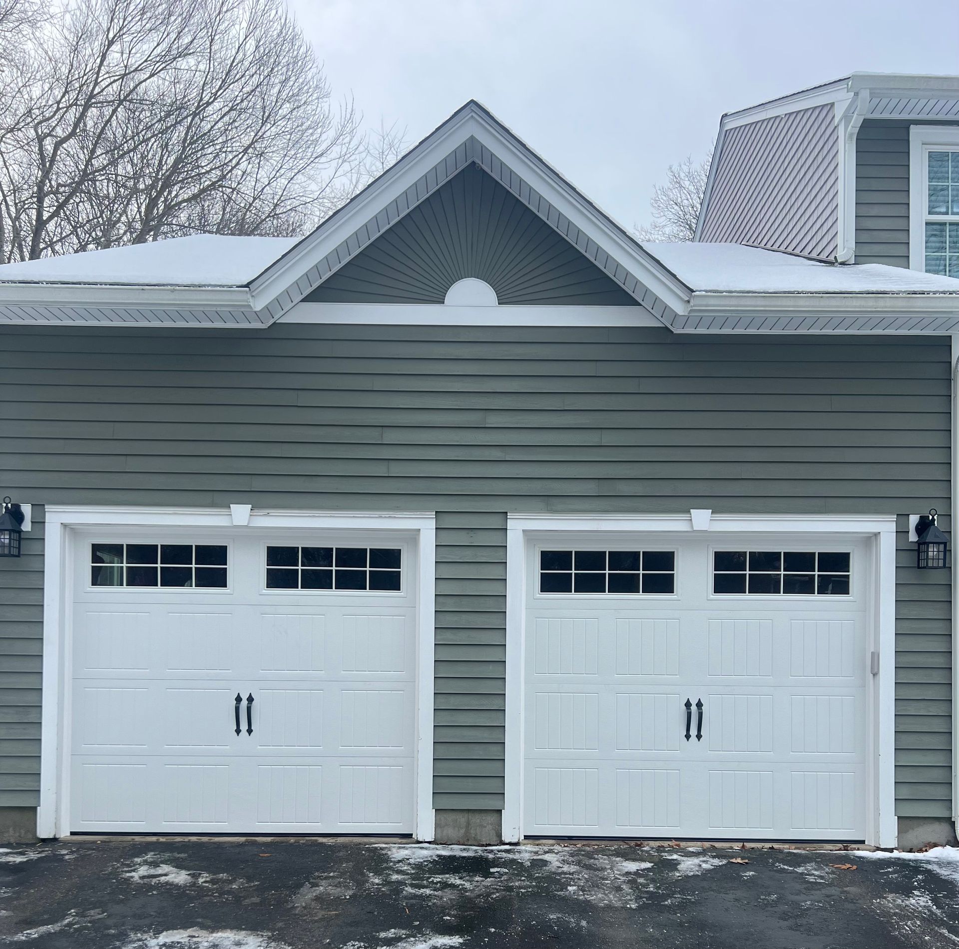 Two-car garage with white doors, green siding, and a snow-covered roof.