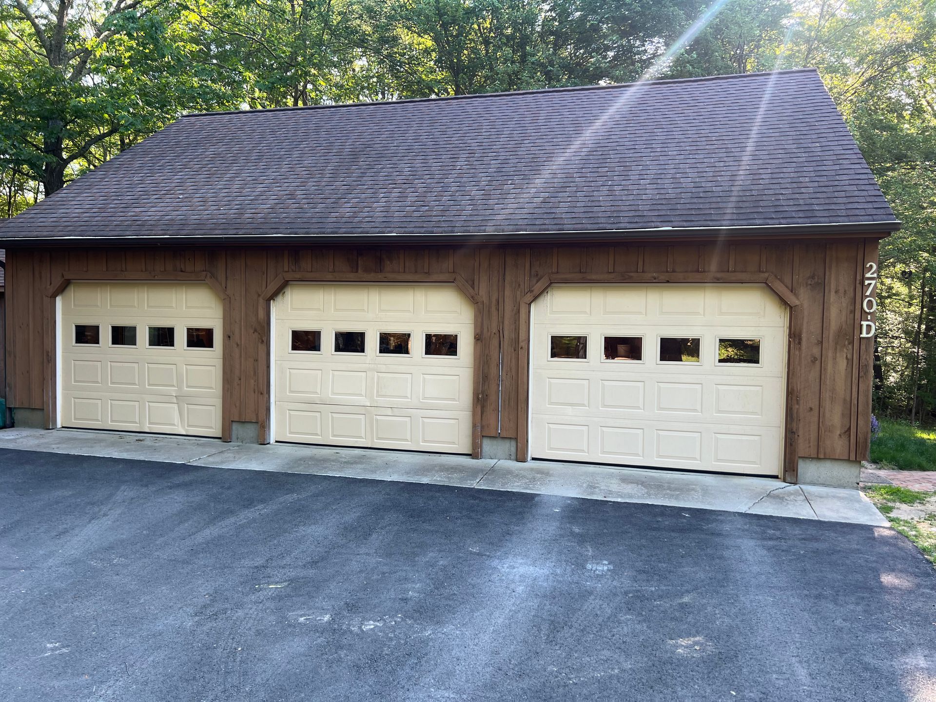Three-car garage with tan doors and a brown roof, set on an asphalt driveway.