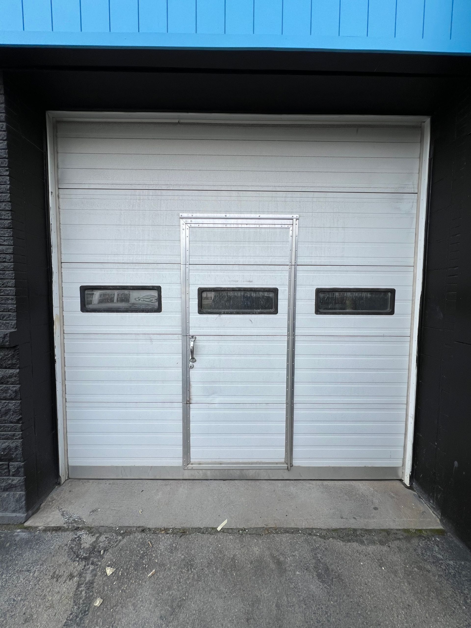 White garage door with an integrated pedestrian door and three rectangular windows.