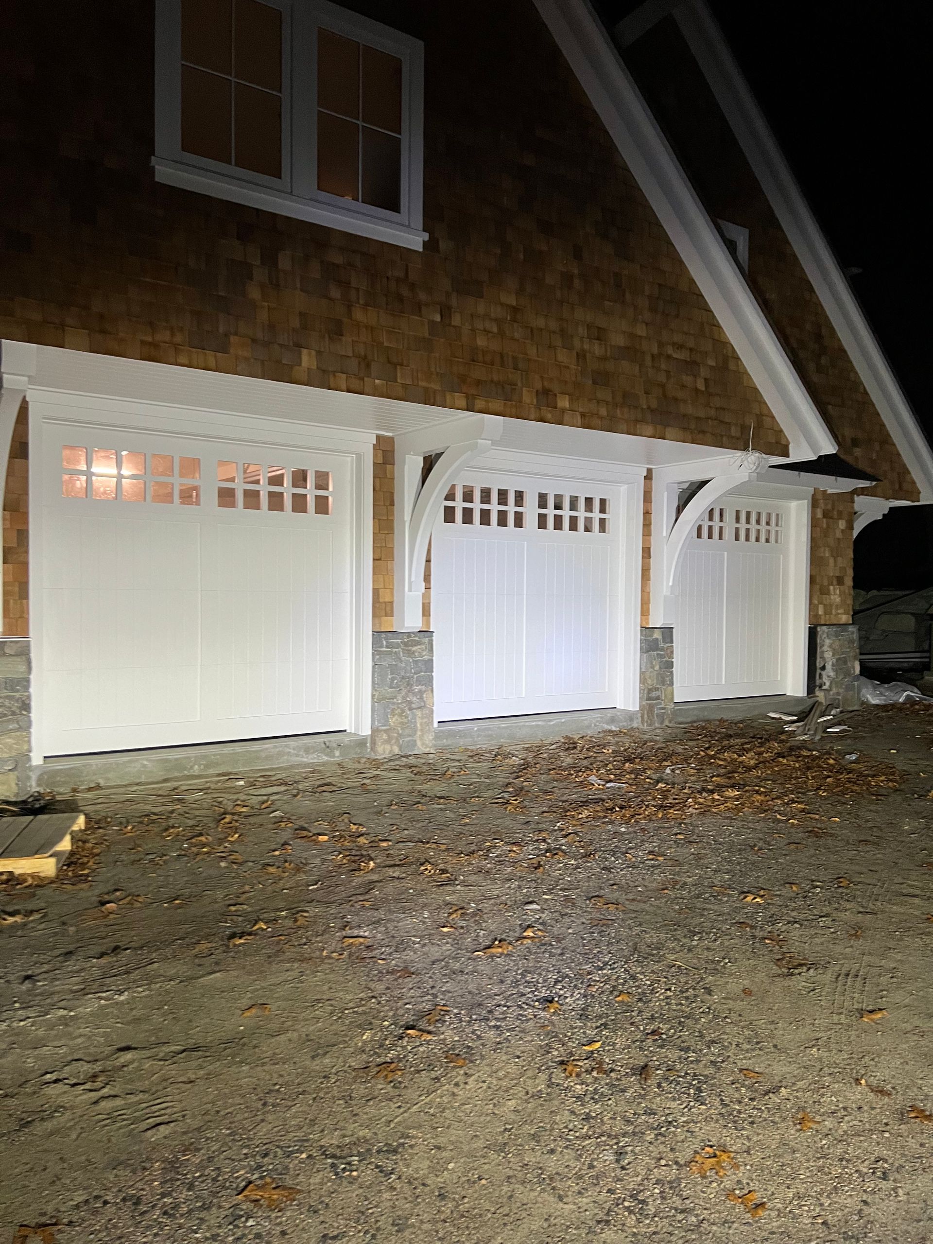 Three white garage doors with arched trim under a shingled roof at night.