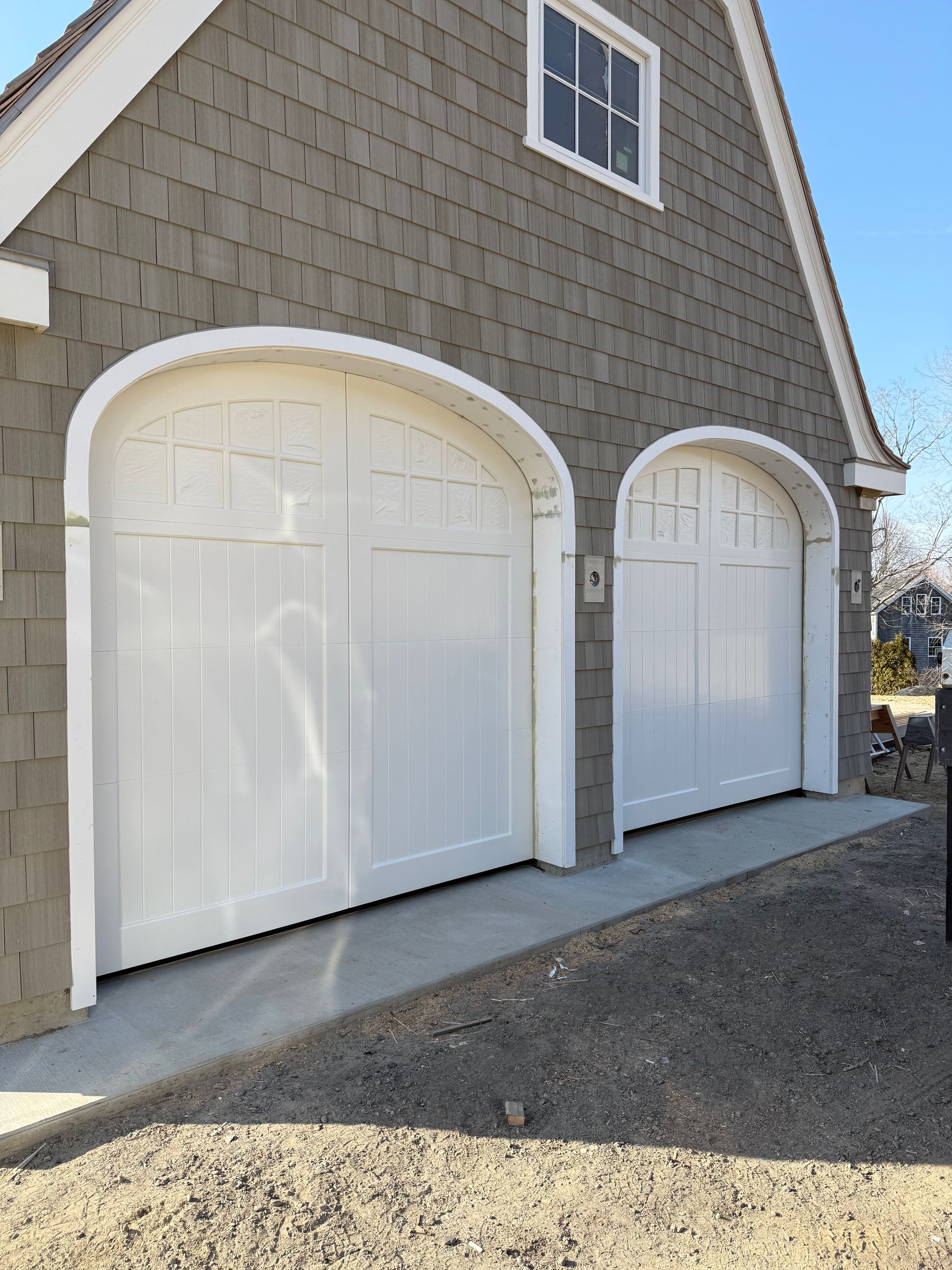 Two white arched garage doors with a concrete driveway on a gray shingled house.