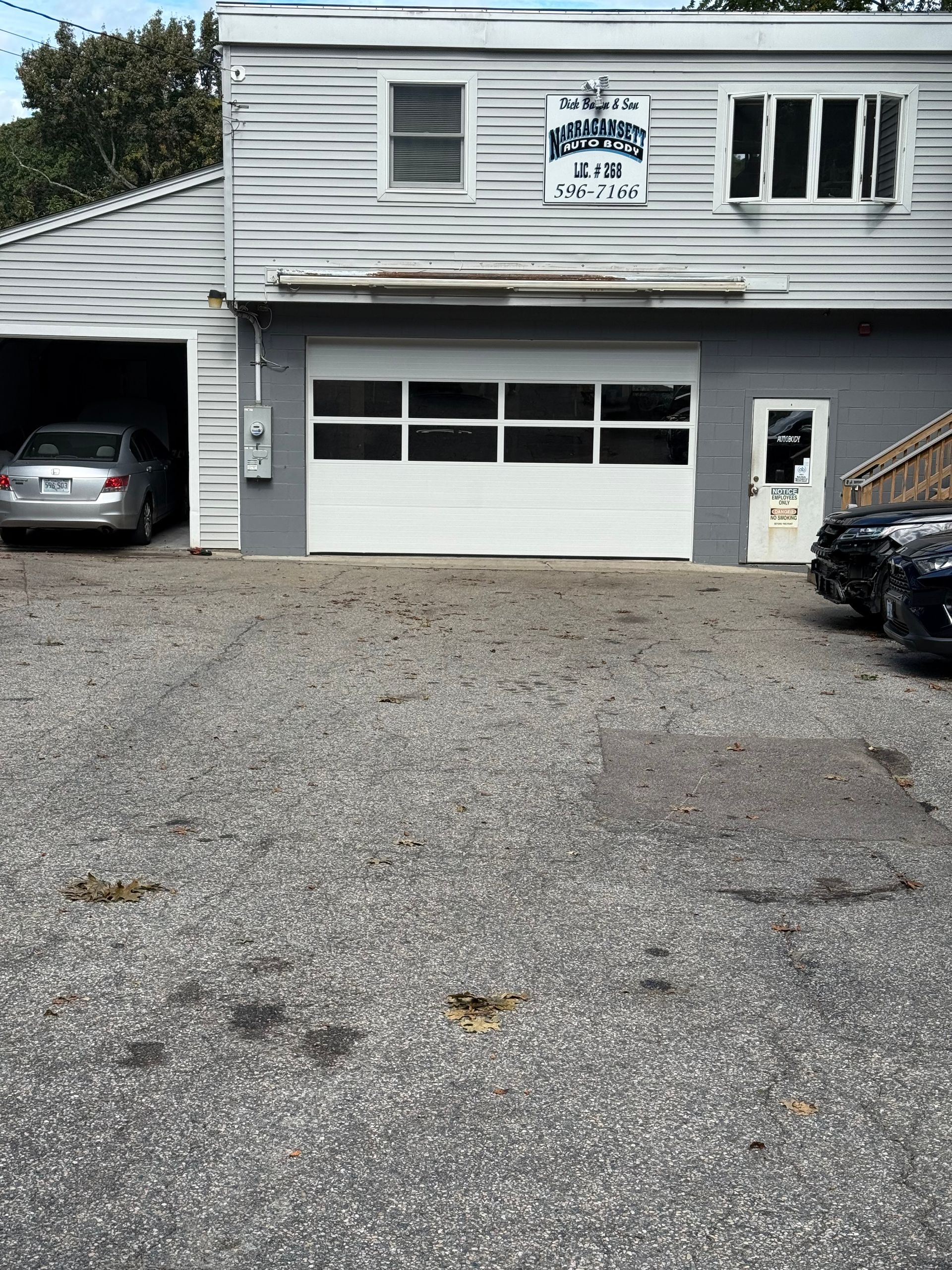Exterior of a gray auto repair shop with a closed garage door and a parked car.